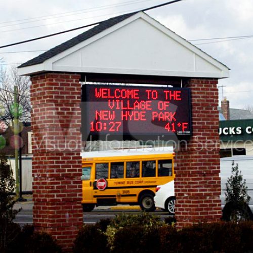 Village welcome sign with school bus nearby.