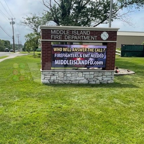 Fire department recruitment sign on grassy lawn.